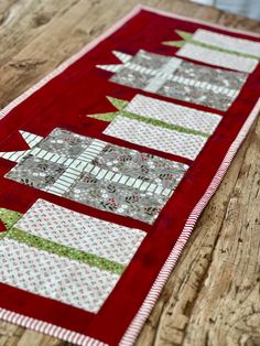 a red table runner with white and green christmas trees on the top, sitting on a wooden surface