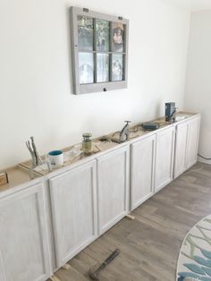 a kitchen with white cabinets and drawers under a window next to a rug on the floor