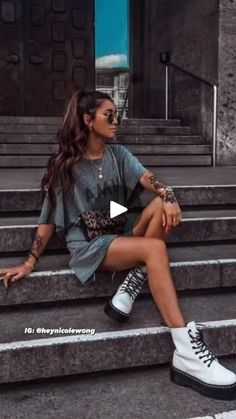 a woman sitting on steps with her legs crossed, wearing white sneakers and a gray dress