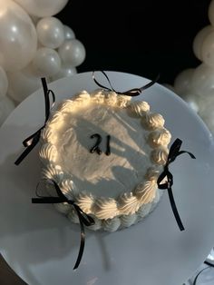 a white cake sitting on top of a white plate covered in icing and black ribbon