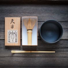 a wooden table topped with a black bowl next to a bamboo whisk