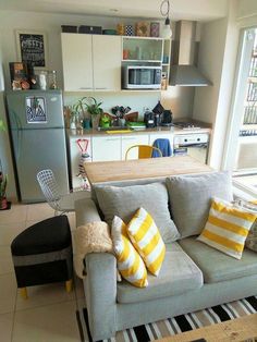 a grey couch with yellow and white pillows in a living room next to a refrigerator