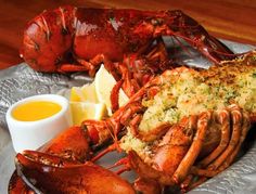 there is a large lobster on the plate with lemon wedges and sauce next to it