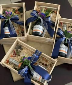 four wine bottles in wooden boxes with blue ribbon and flowers on the top one is empty