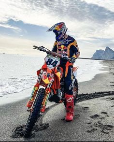 a man riding on the back of a dirt bike down a sandy beach next to the ocean