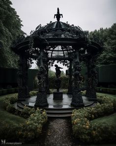 a gazebo in the middle of a garden with statues on it's sides