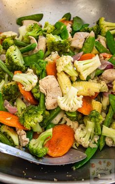 a metal bowl filled with broccoli, carrots and other veggies