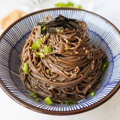 a blue and white bowl filled with noodles, sesame seed sprouts and seaweed