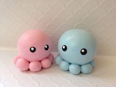 two small toys sitting next to each other on a white tableclothed surface, one is blue and the other is pink