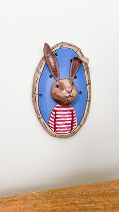 a paper cutout of a rabbit wearing a striped shirt on a white wall above a wooden table