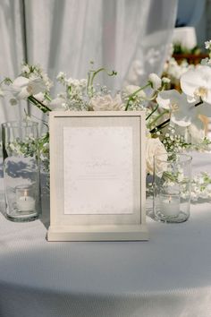 a table topped with vases filled with white flowers and greenery next to a sign