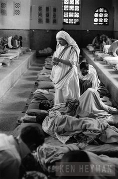 several people are sitting on the floor in a room with many cots and mattresses