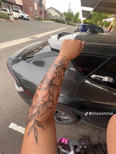 a person with a tattoo on their arm next to a parked car in a parking lot