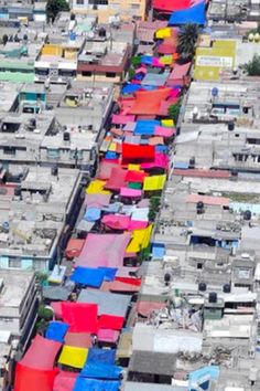 an aerial view of a city with lots of colorful umbrellas hanging from the buildings