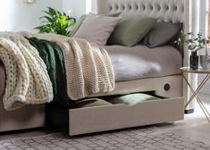 a bed with an open drawer underneath it in a room next to a table and potted plant