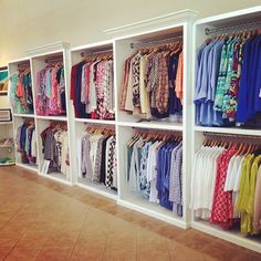 the closet is full of colorful clothing and clothes hanging on white shelving unit shelves