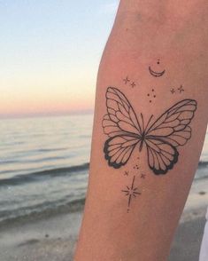 a person with a butterfly tattoo on their arm near the ocean and stars in the sky