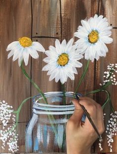 someone is painting daisies in a mason jar on the side of a wooden wall