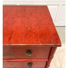 an old red chest with marbled top and brass hardware on the bottom, sitting in front of a white door