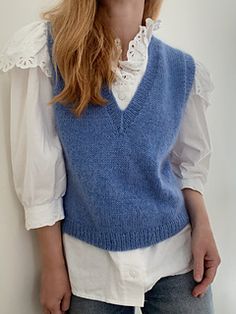 a woman wearing a blue sweater vest and white shirt is standing in front of a wall