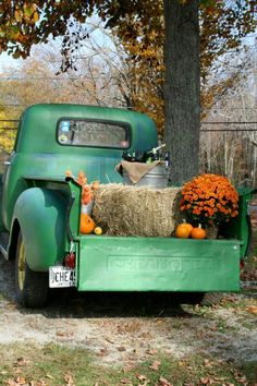 an old green truck with hay and pumpkins in the bed is parked next to a tree