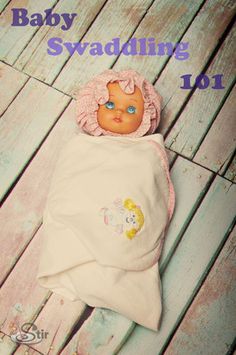 a baby doll laying on top of a wooden floor next to a white blanket with the words baby swaddling 101