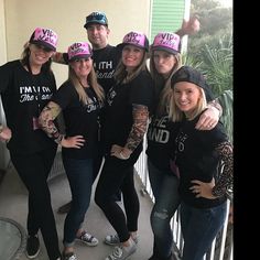 a group of women standing next to each other on a porch wearing pink hats and black shirts