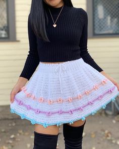 a woman wearing a black top and white crochet skirt with pink flowers on the bottom