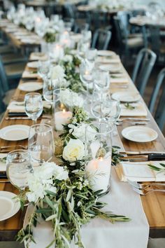 a long table is set with white flowers and greenery for an elegant dinner party