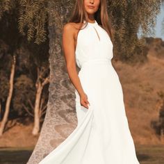 a beautiful woman in a white dress posing for a photo with an olive tree behind her