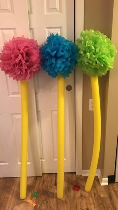 three tall yellow poles with colorful flowers on them in front of a white door and wooden floor