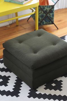 a green ottoman sitting on top of a black and white rug next to a yellow table