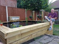 a man sitting on top of a wooden bench next to a small fish pond in a backyard