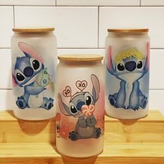 three glass jars with cartoon characters painted on them sitting on a wooden shelf next to a tiled wall