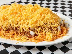 a white plate topped with spaghetti and cheese covered in grated cheese on a black and white checkered tablecloth