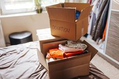 an open cardboard box sitting on top of a bed with clothes in it and the word donation written on its side