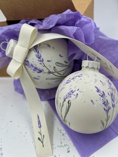 two white ornaments with purple flowers on them and a ribbon tied around the ornament