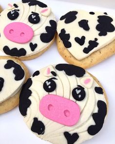 four decorated cookies in the shape of cows on a white plate with pink and black frosting