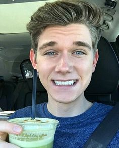 a man holding a green smoothie in his hand and smiling at the camera while sitting in a car