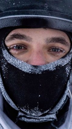 a man wearing a black hat and scarf with snow on it's face is looking at the camera