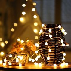 a table topped with a basket filled with white lights next to a vase full of flowers