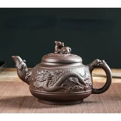 a teapot with a dragon design on the lid and handle is sitting on a table