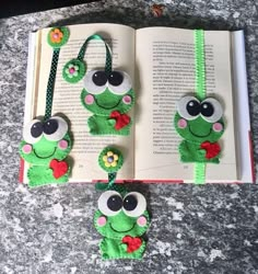 two bookmarks made to look like frogs with eyes and ears, hanging from a book