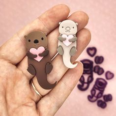 someone holding two cute little animal brooches in their hands, one is brown and the other is white