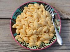 a bowl filled with macaroni and cheese on top of a wooden table next to a fork