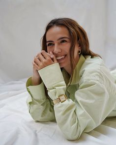 a woman laying on top of a bed next to a white sheet covered wall with her hands under her chin