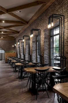 an empty restaurant with wooden tables and black chairs, brick walls and exposed ceilinging