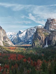 the mountains are covered in snow and trees with fall colored leaves on them, as well as a waterfall