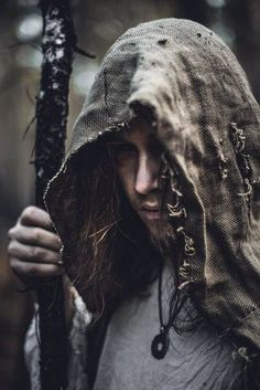 a man with long hair wearing a hooded jacket and holding a stick in his hands