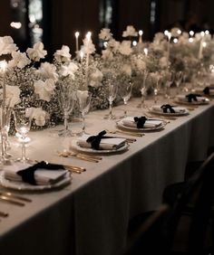 a long table is set with white flowers and silverware for an elegant dinner party